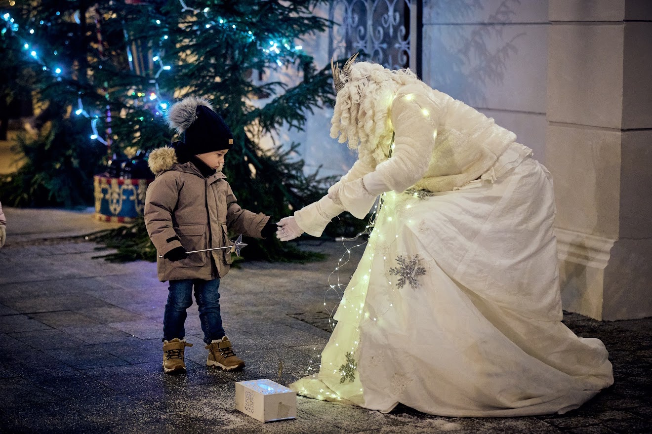 Kobieta w białym przebraniu podaje rękę chłopcu