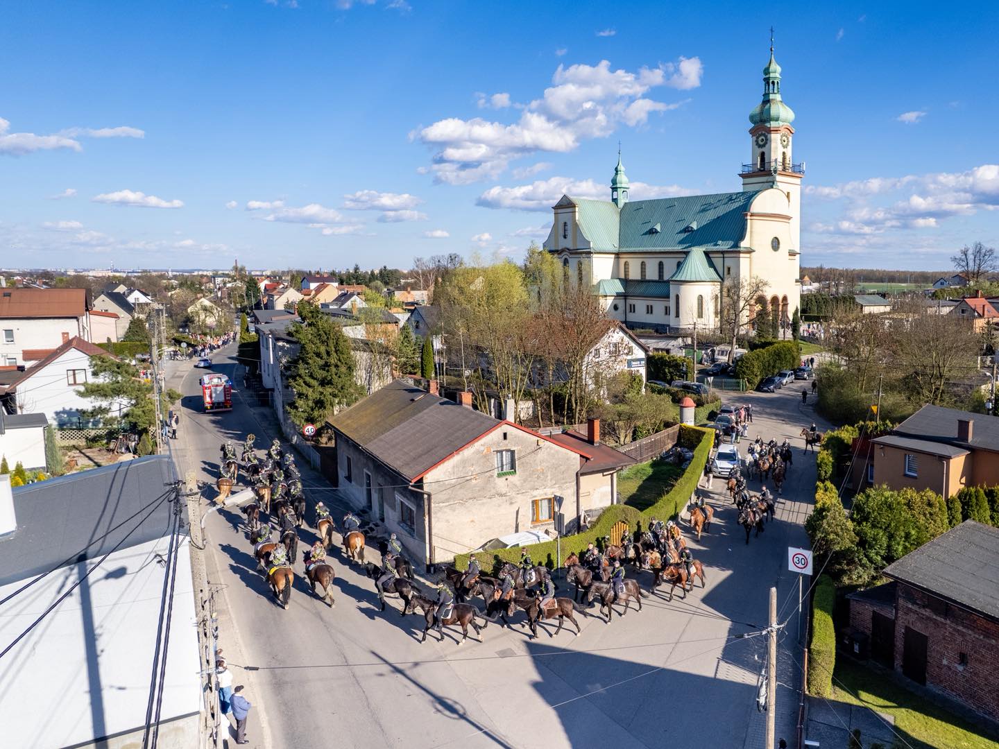 Procesja konna, ujęcie z góry. W oddali widać wieżę kościoła w Ostropie