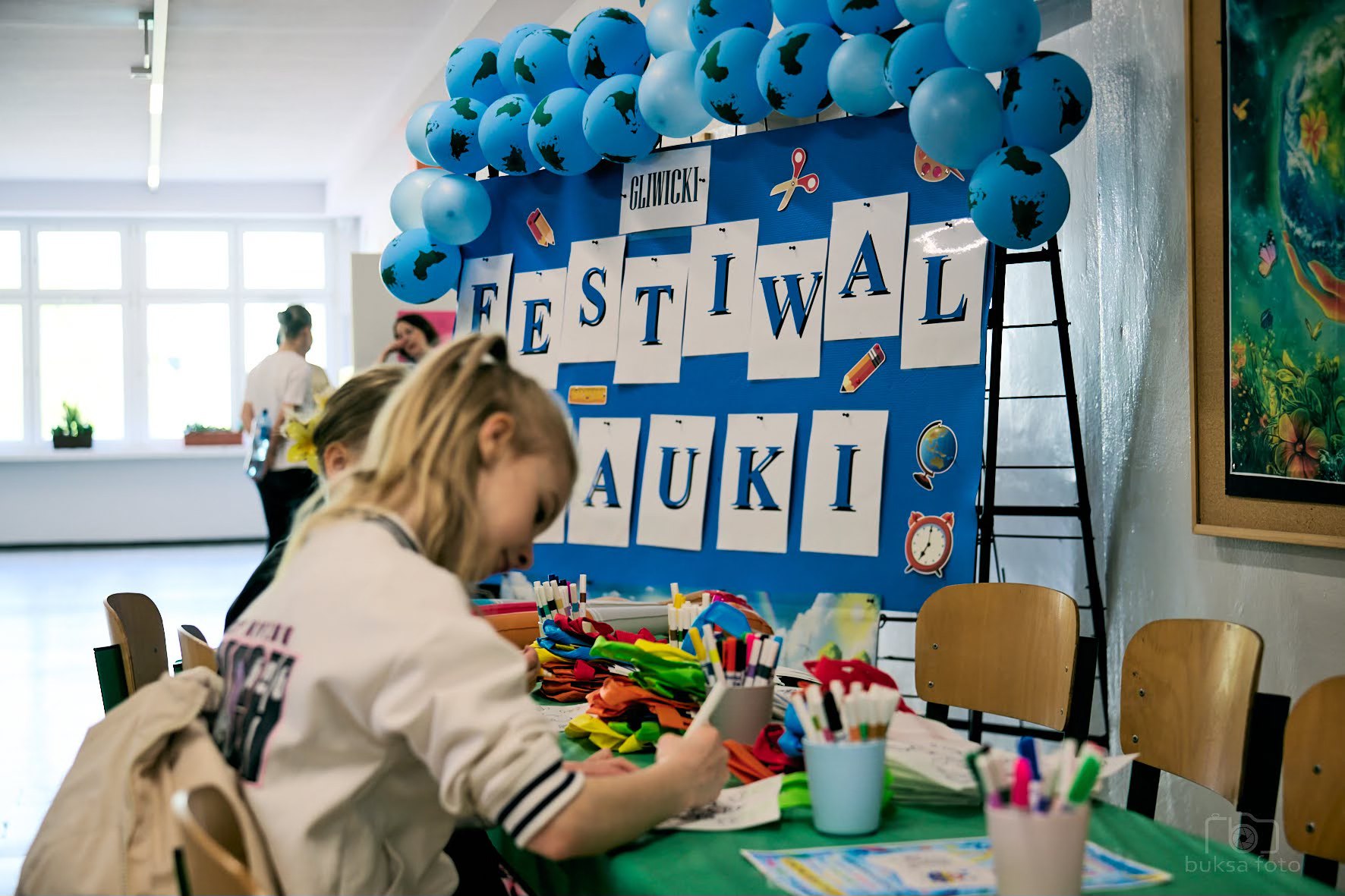 dziewczynki siedzą w ławce, obok napis Festiwal Nauki