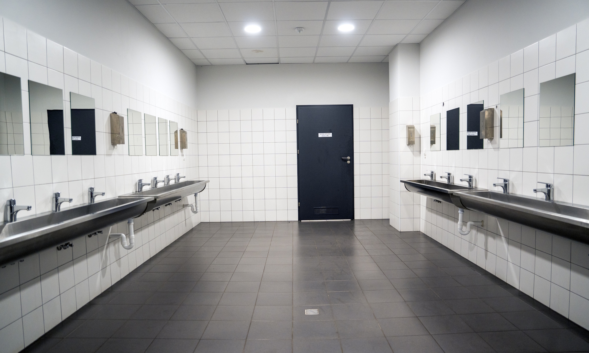 łazienka z umywalkami i białymi kaflami na ścianach oraz grafitową podłogą