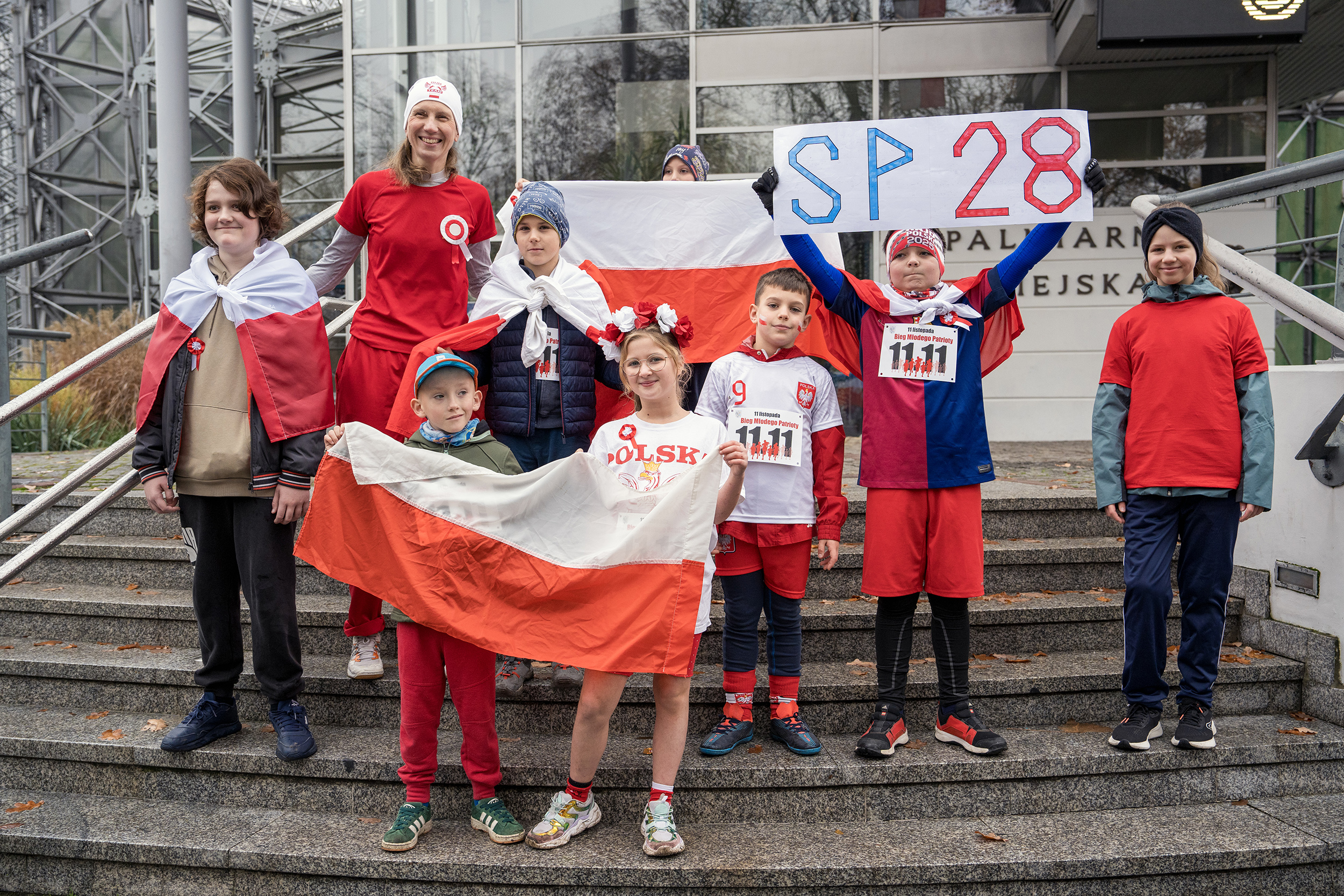 Uczniowie SP 28 w biało-czerwonych strojach na schodach Palmiarni podczas Biegu Młodego Patrioty