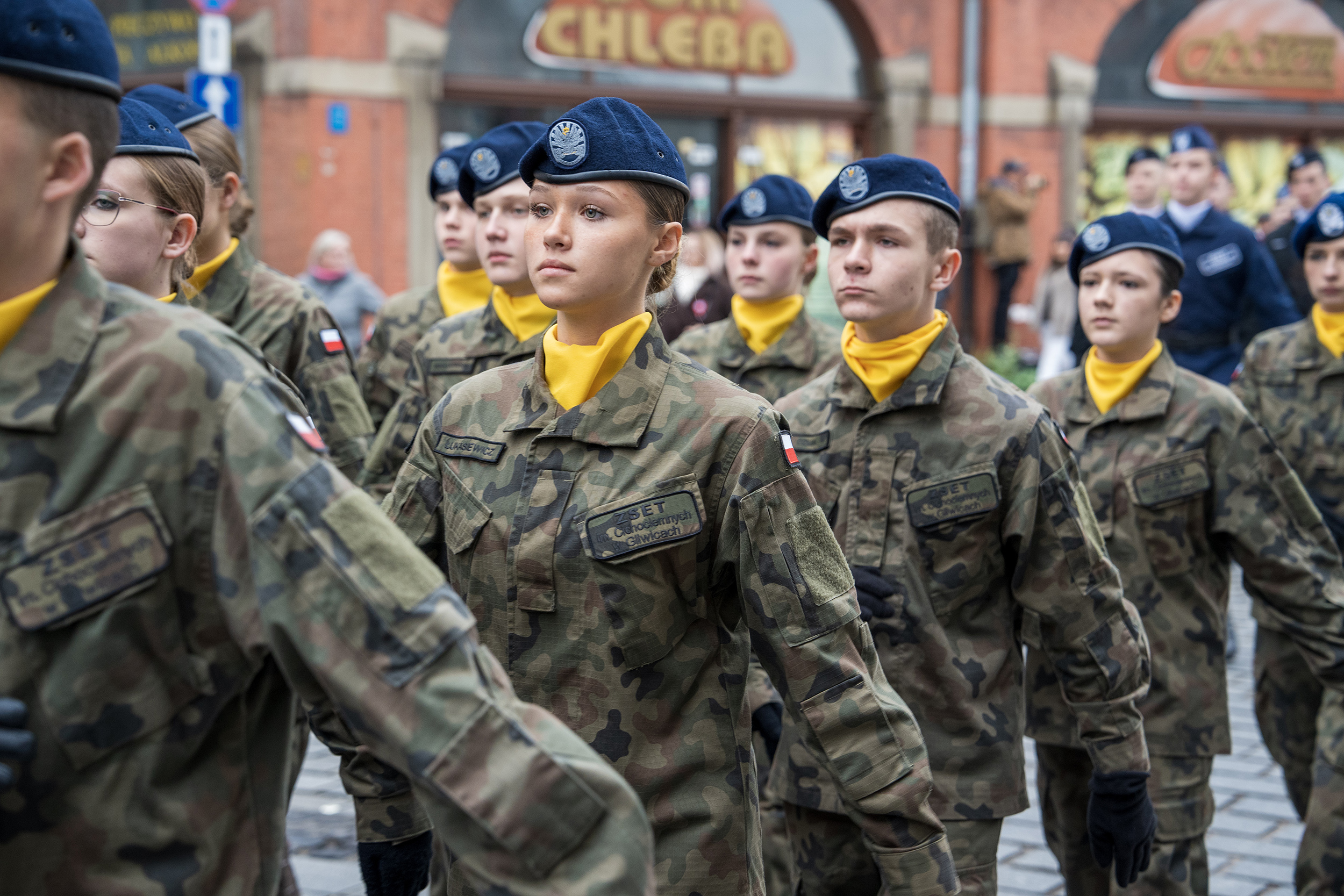 Przemarsz przez miasto z flagą Polski. Na pierwszym planie maszerująca klasa mundurowa.
