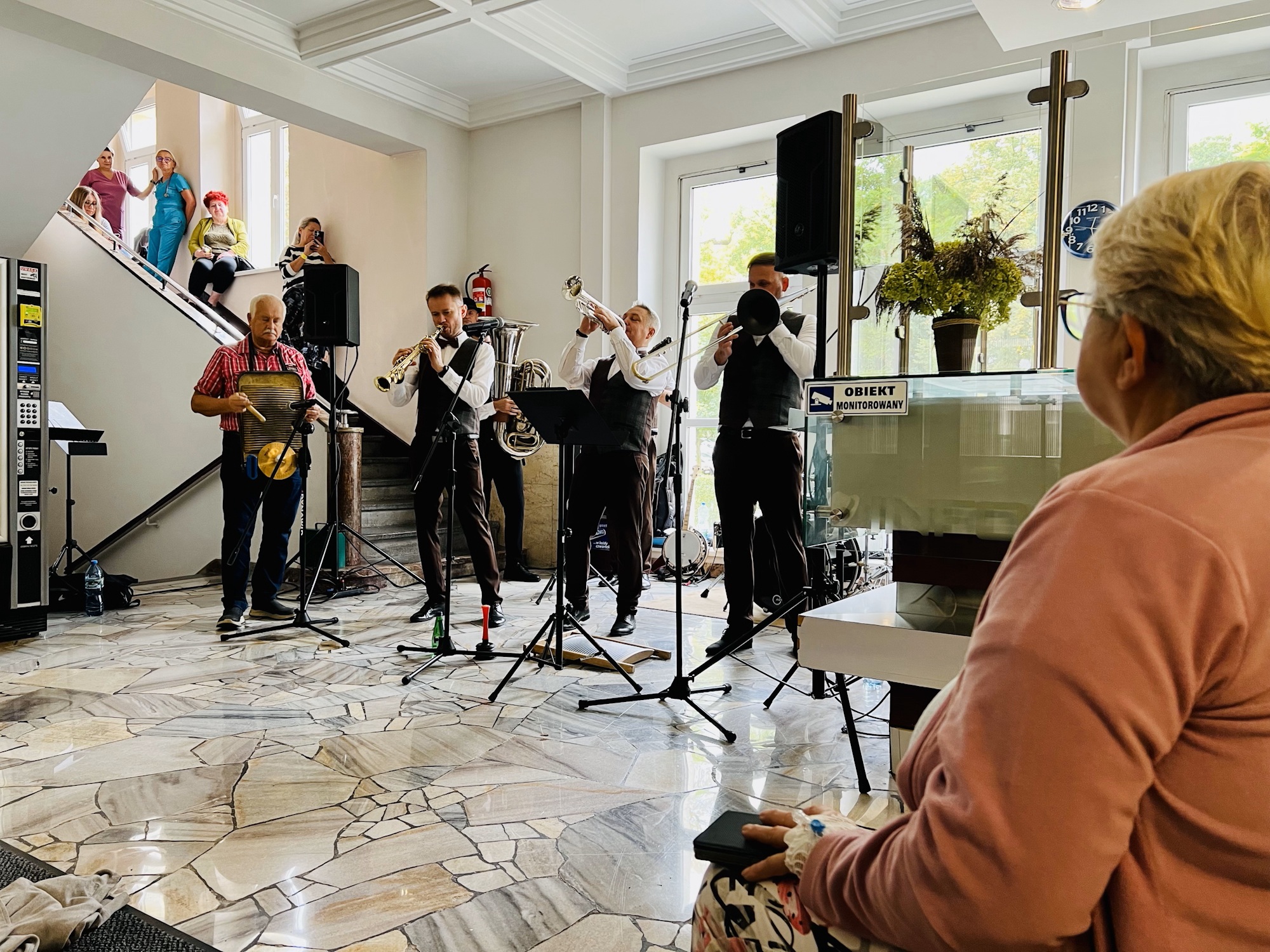 muzycy na korytarzu. Pacjenci siedzą i słuchają