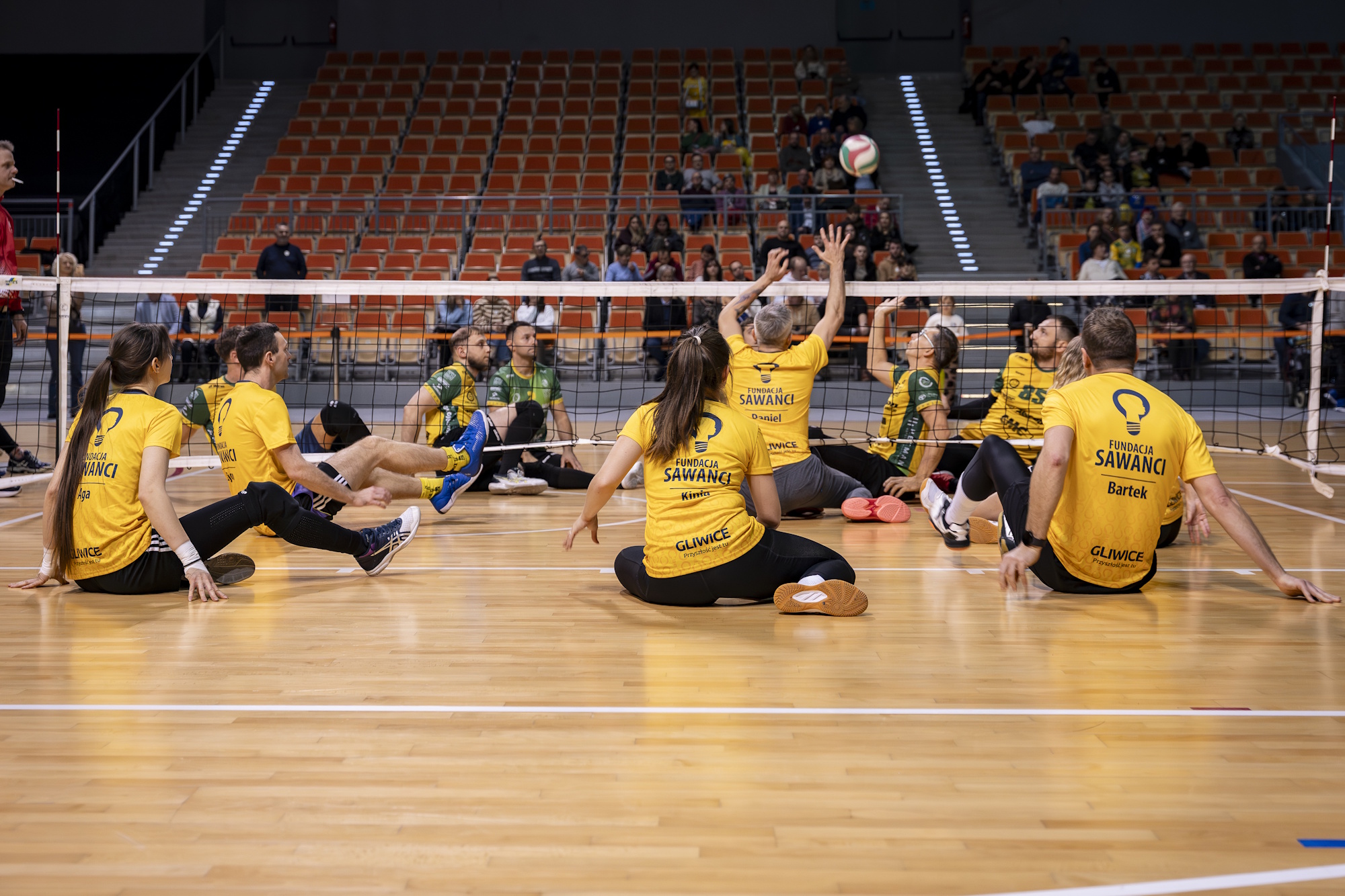 sportowcy w żółtych koszulkach siedzą na podłodze