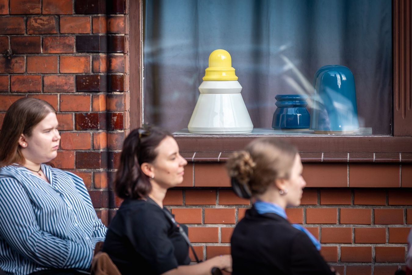 Trzy siedzące osoby przed wystawą urn 