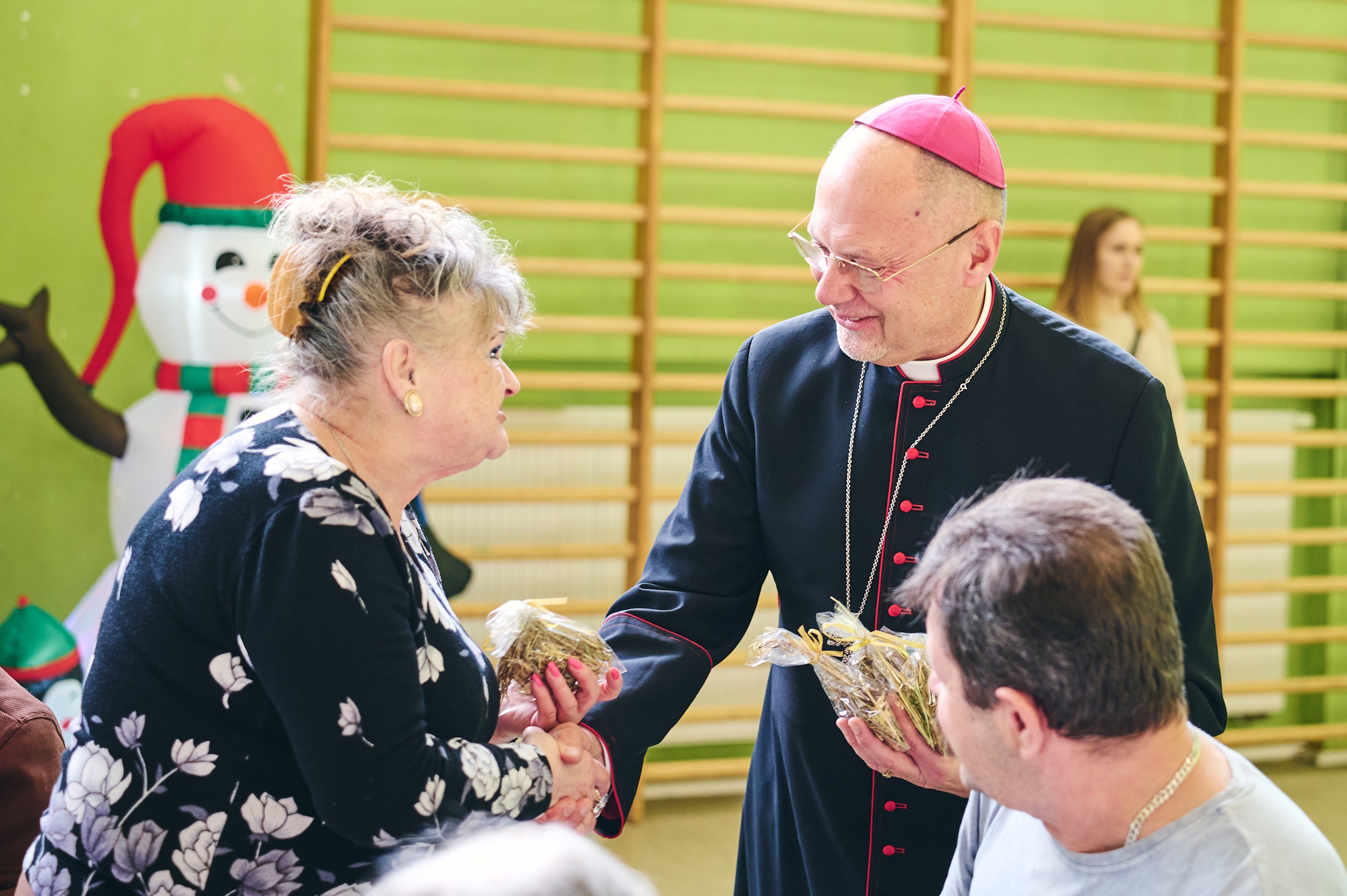 Biskup wręczający starszej pani sianko pod obrus