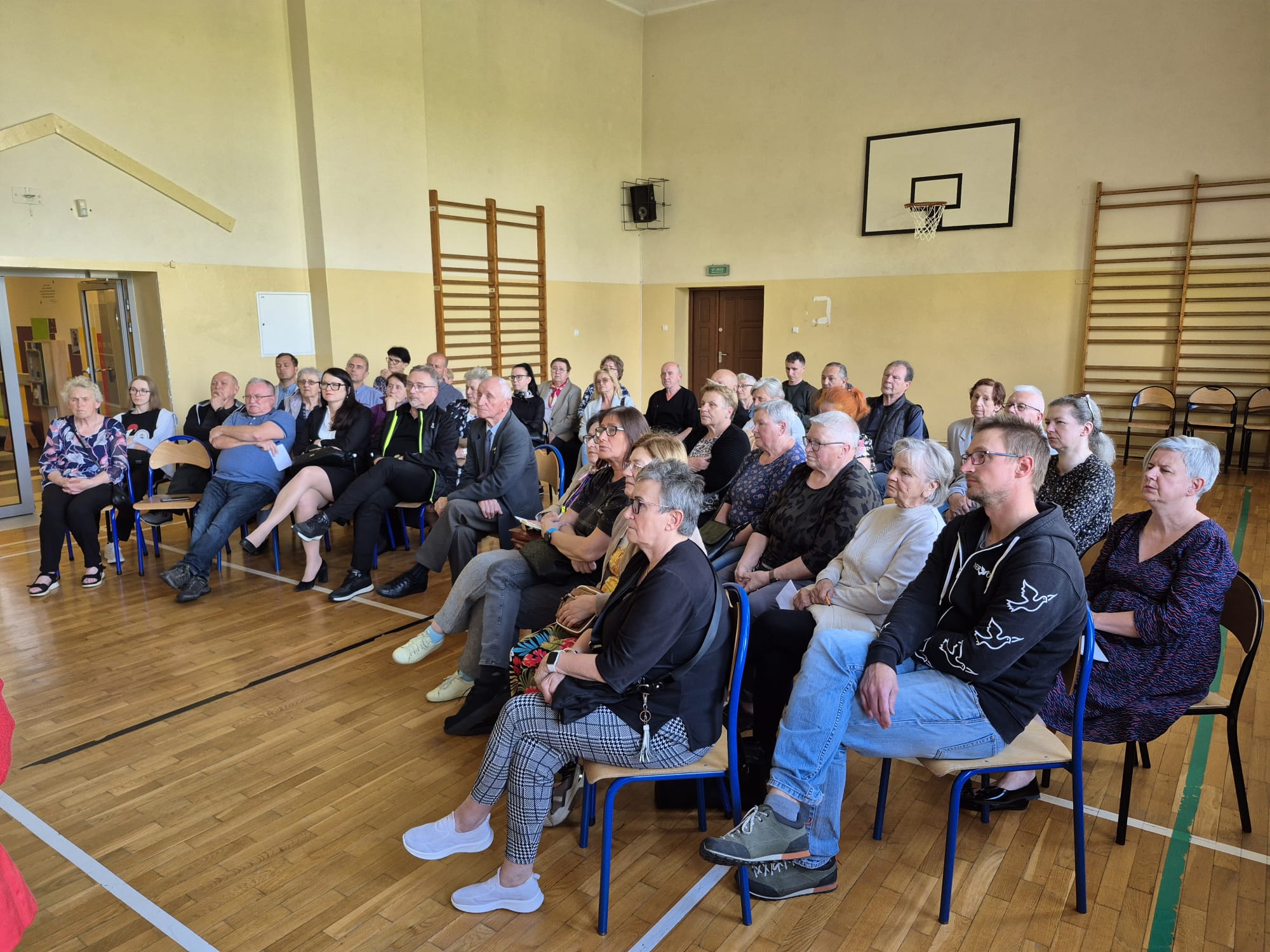 ludzie siedzący na krzesłach i zadający pytania podczas spotkania konsultacyjnego w Brzezince