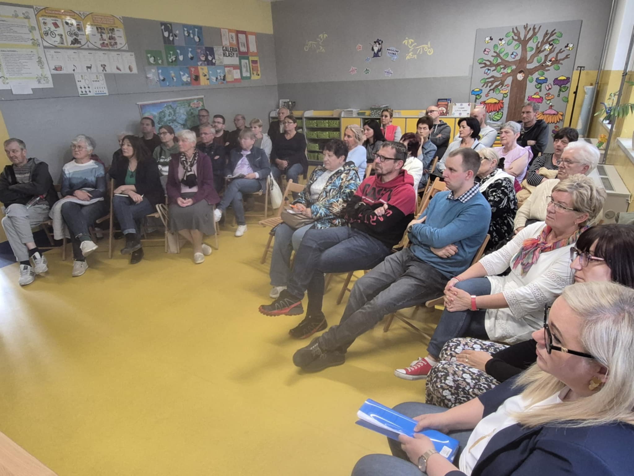 ludzie siedzący na krzesłach i zadający pytania podczas spotkania konsultacyjnego w Wilczym Gardle