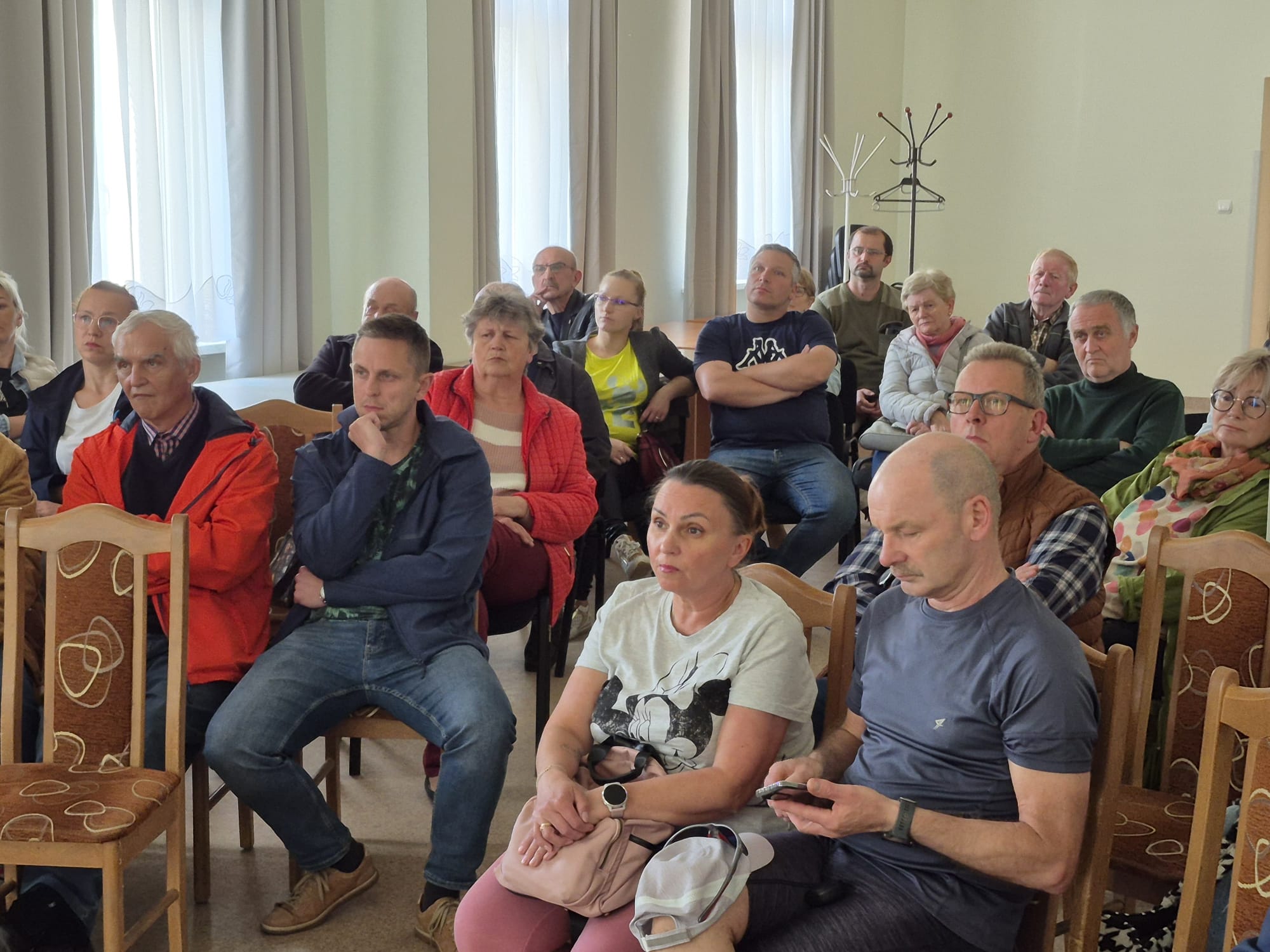 ludzie siedzący na krzesłach i zadający pytania podczas spotkania konsultacyjnego w Czechowicach