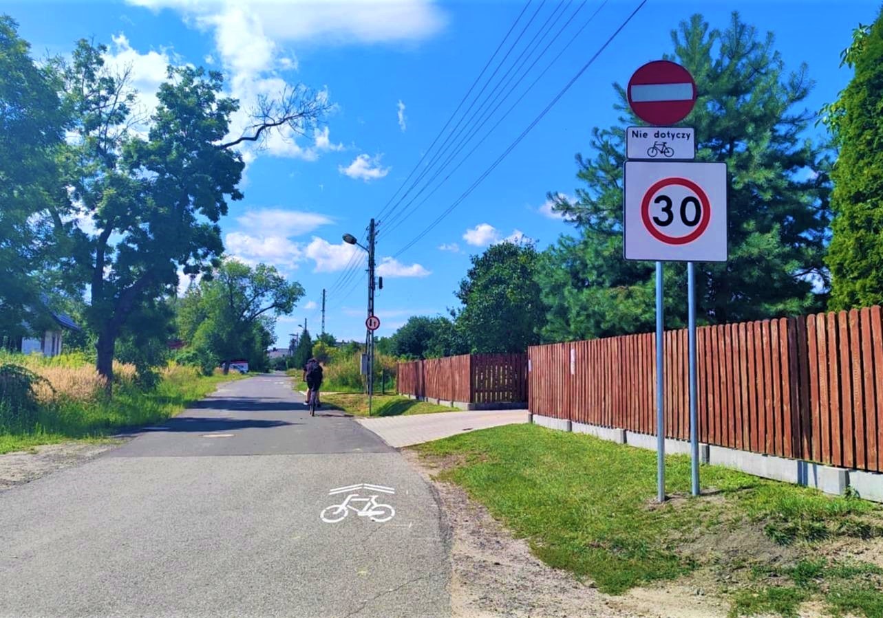 Kontraruch rowerowy wyznaczony na wąskiej asfaltowej drodze, na pierwszym planie znaki ograniczenie prędkości do 30 km na godzinę, zakaz wjazdu nie dotyczy rowerów