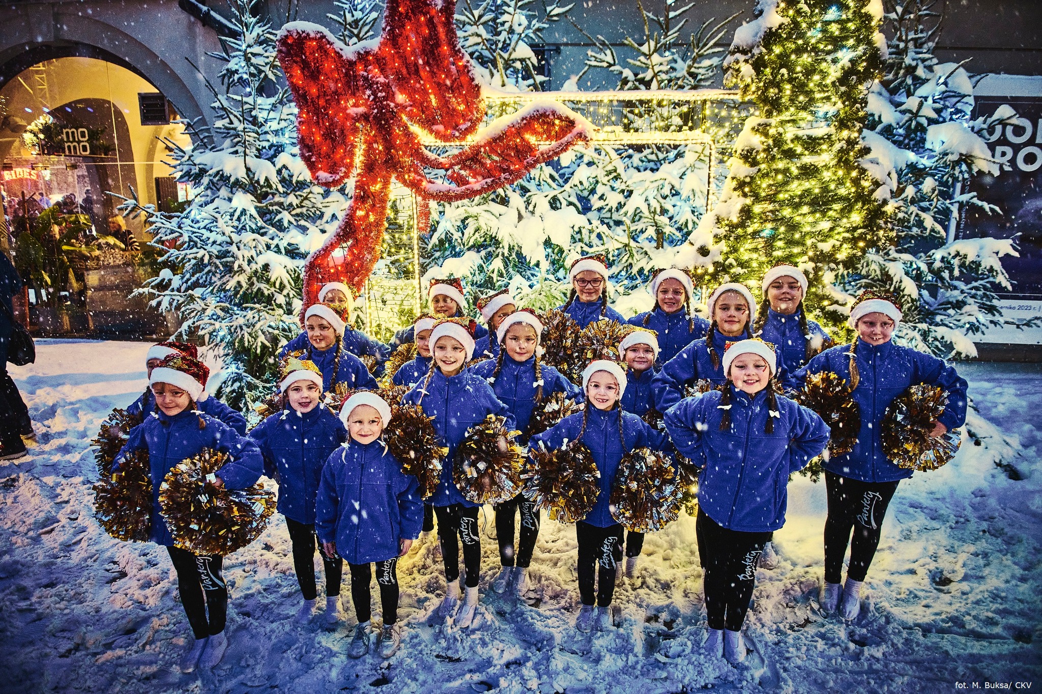 dziewczynki w granatowych bluzach i z pomponami na Rynku, w tle świetlisty prezent