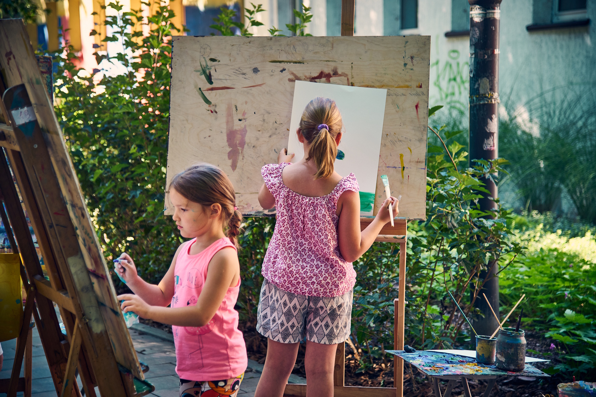 Dwie dziewczynki malują przy stzalugach w plenerze