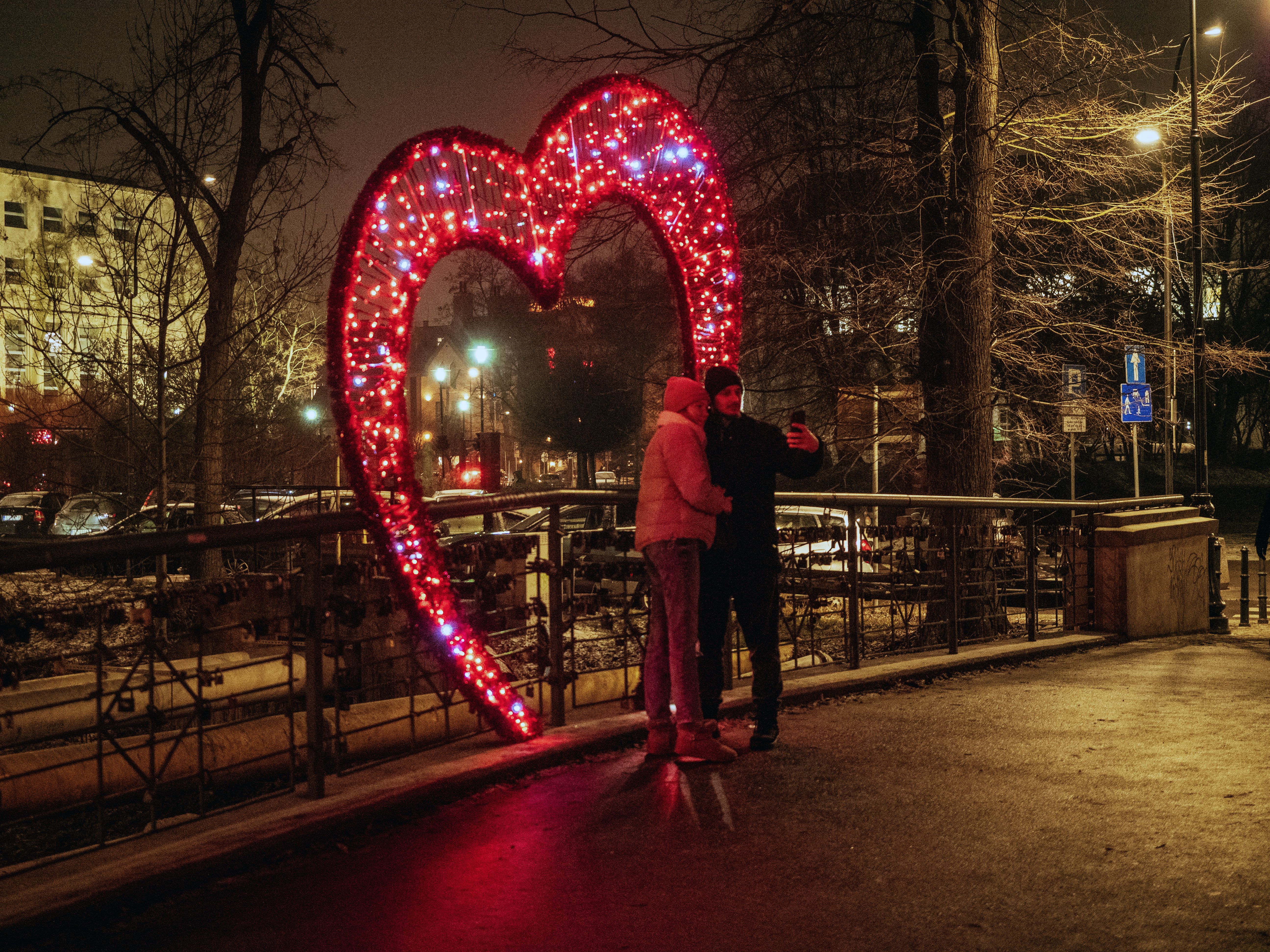 Dwoje ludzi robi sobie zdjęcie przy walentynkowej dekoracji w kształcie serca