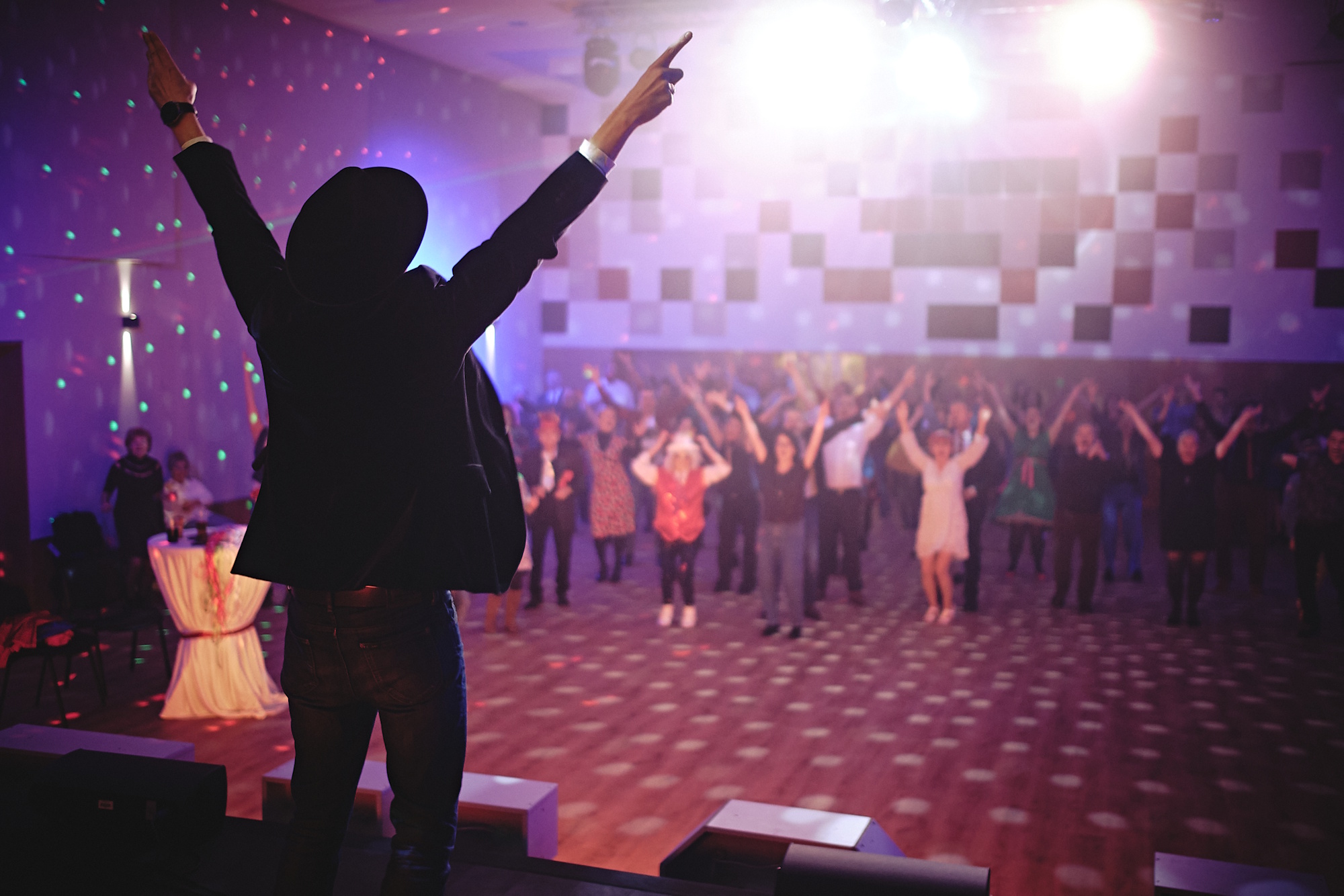 Człowiek z uniesionymi rękami stoi na scenie, przed sceną ludzie z uniesionymi rękami