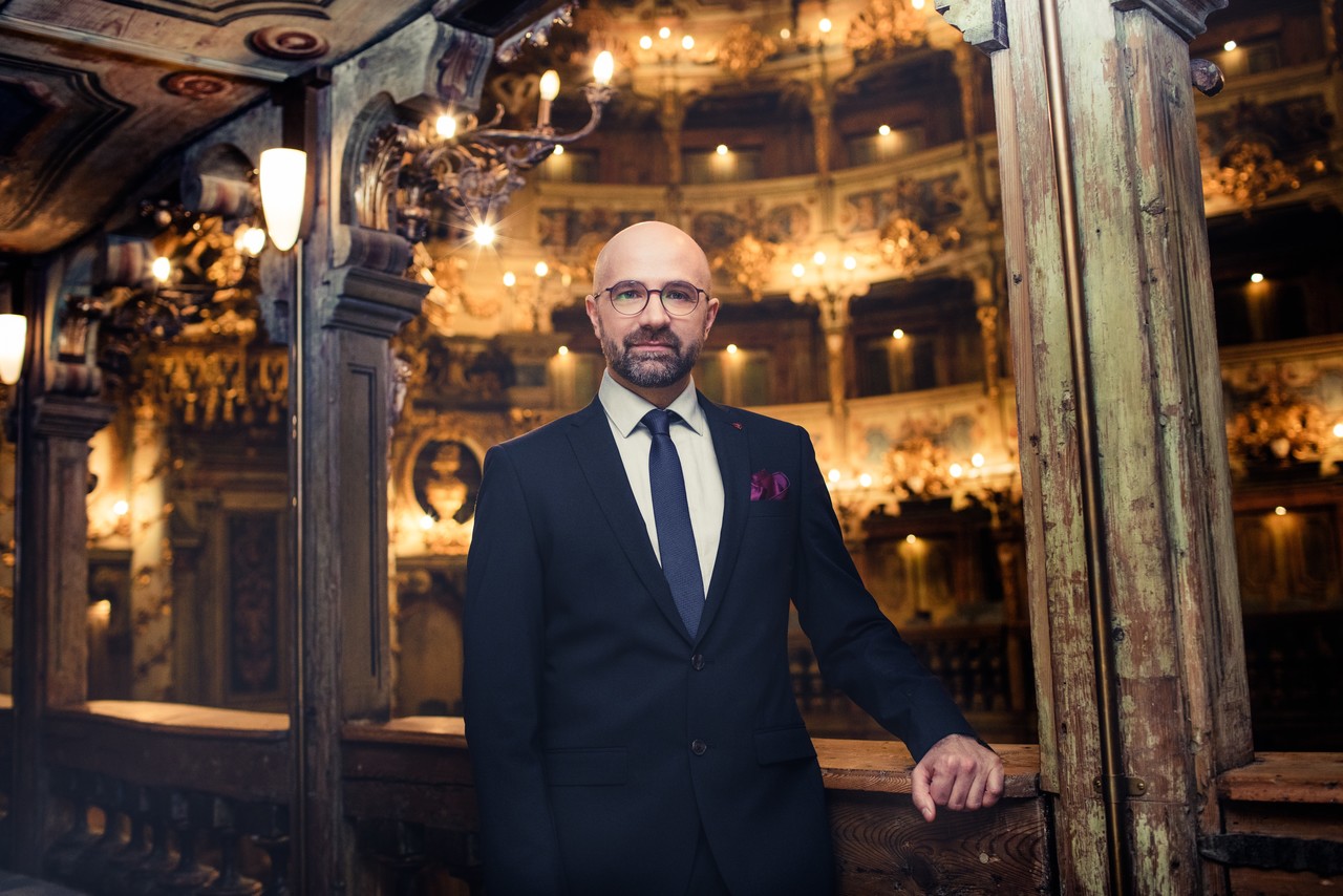 mężczyzna w teatrze, elgancko ubrany, w okularach, między kolumnami na balkonie